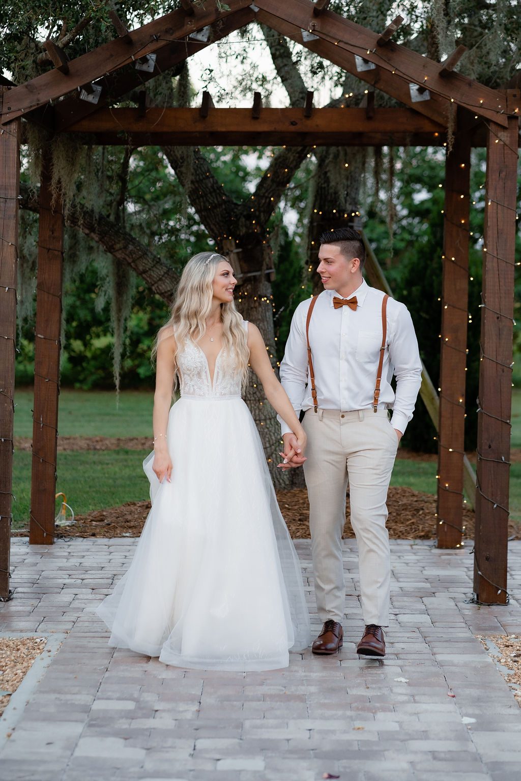 Bride and groom walking under a lit pergola at dusk, captured by Precious Pics Production